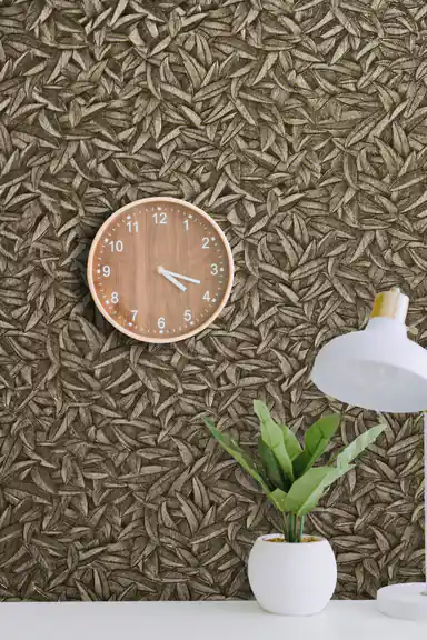 Installed wall of metallic bronze leaf pattern wallpaper with a round wooden clock and desk lamp