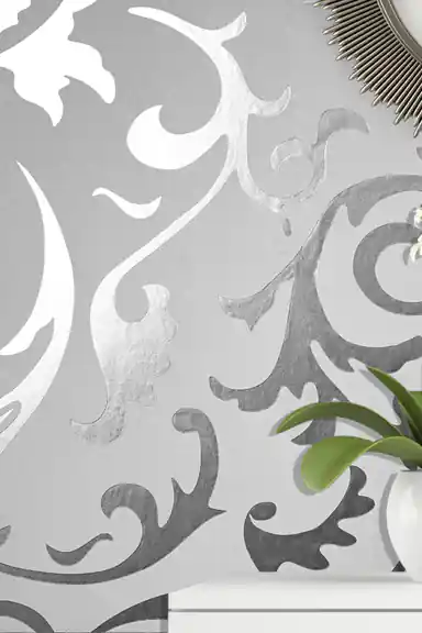 Close-up of silver scrollwork pattern wallpaper with a plant visible in the corner