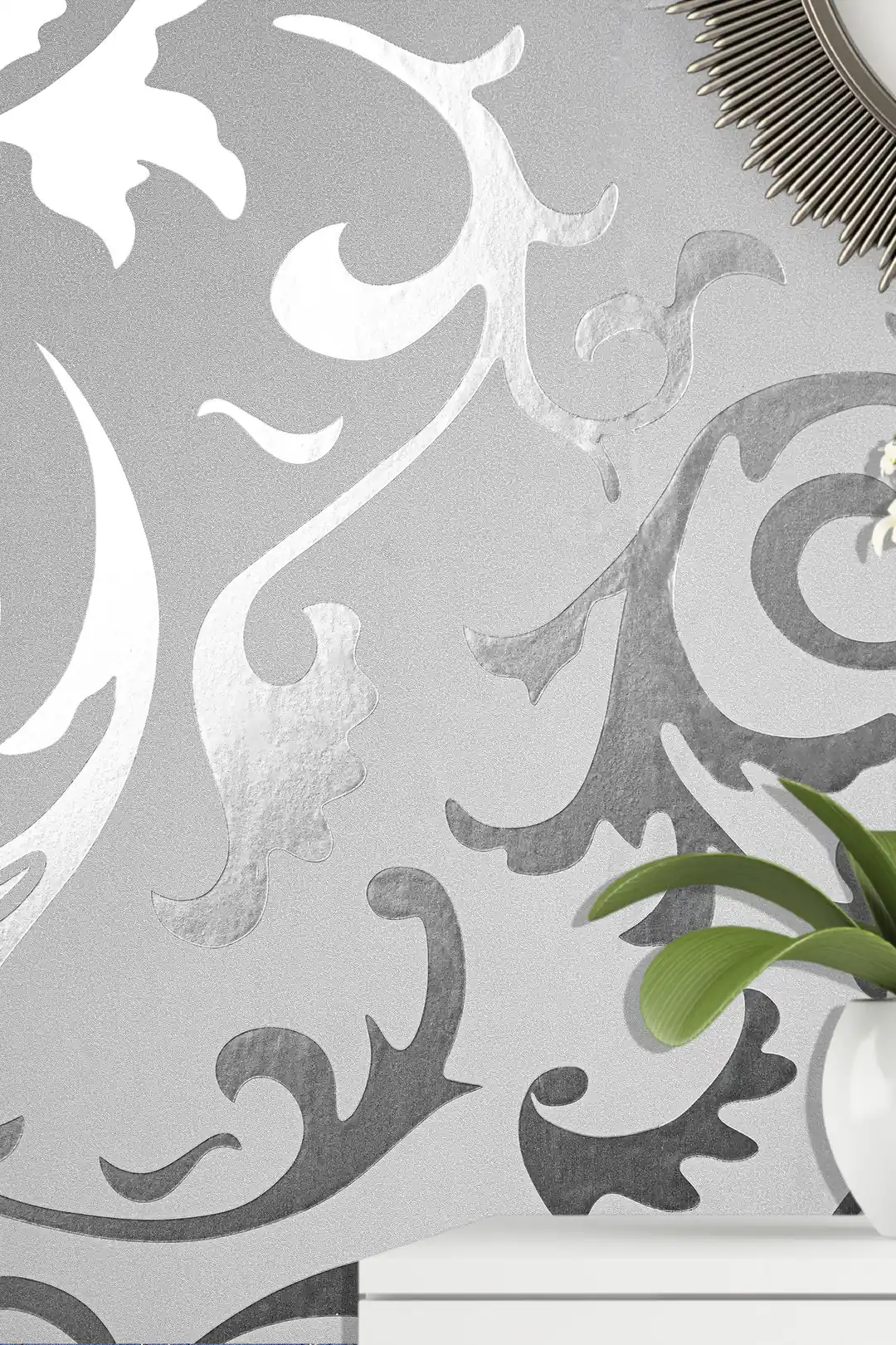 Close-up of silver scrollwork pattern wallpaper with a plant visible in the corner