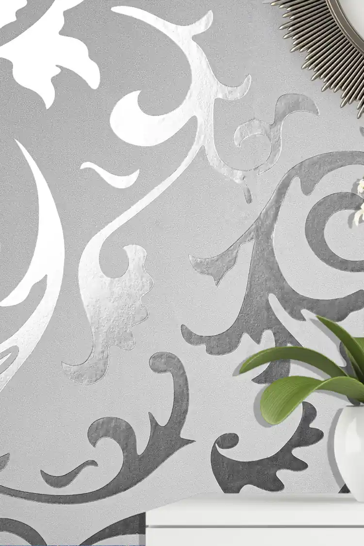 Close-up of silver scrollwork pattern wallpaper with a plant visible in the corner