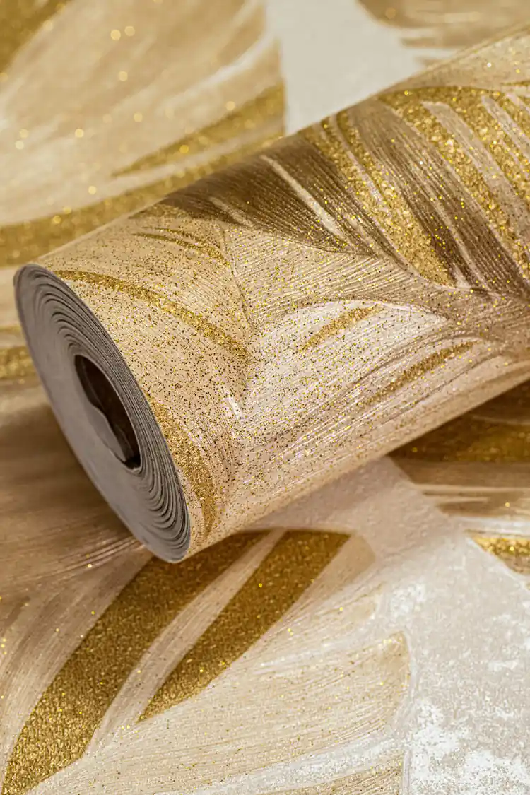 Wallpaper roll showing tropical palm leaves with gold glitter sparkle on a warm beige background