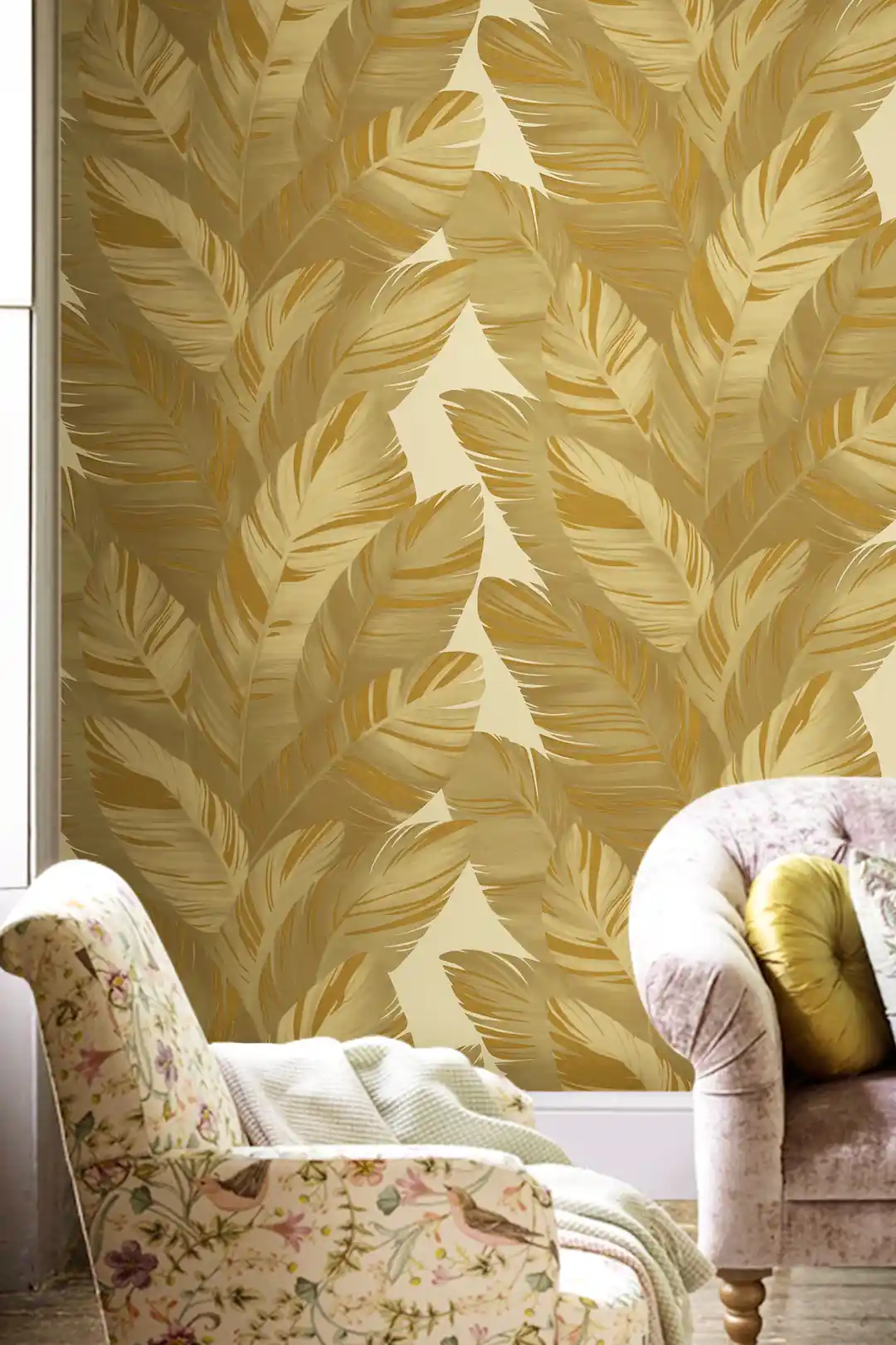 Living room with golden feather-like palm leaf wallpaper pattern behind a floral armchair and pink velvet sofa