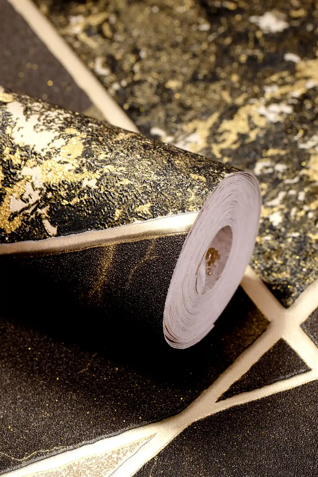 Wallpaper roll of black geometric marble triangles with golden lines resting on the unrolled pattern