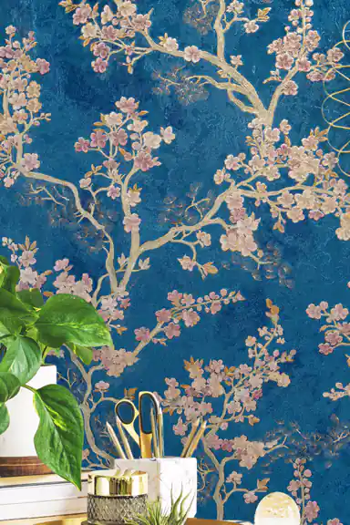 Installed wall of pink cherry blossoms and golden branches on blue wallpaper with desk supplies below