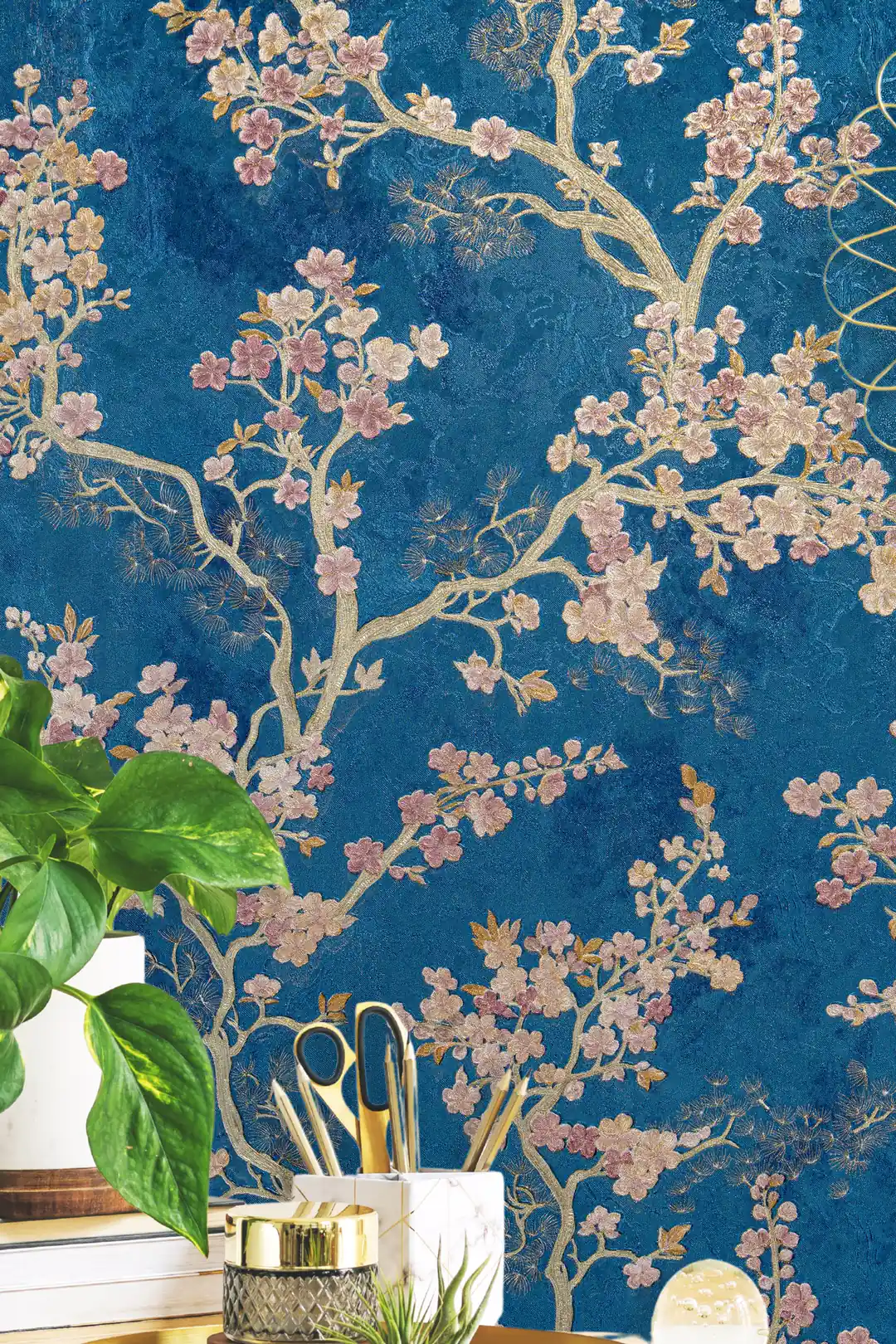 Installed wall of pink cherry blossoms and golden branches on blue wallpaper with desk supplies below