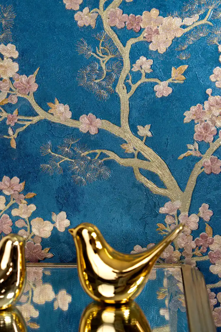 Close-up of golden branches and pink blossoms with a gold bird figurine on blue wallpaper background