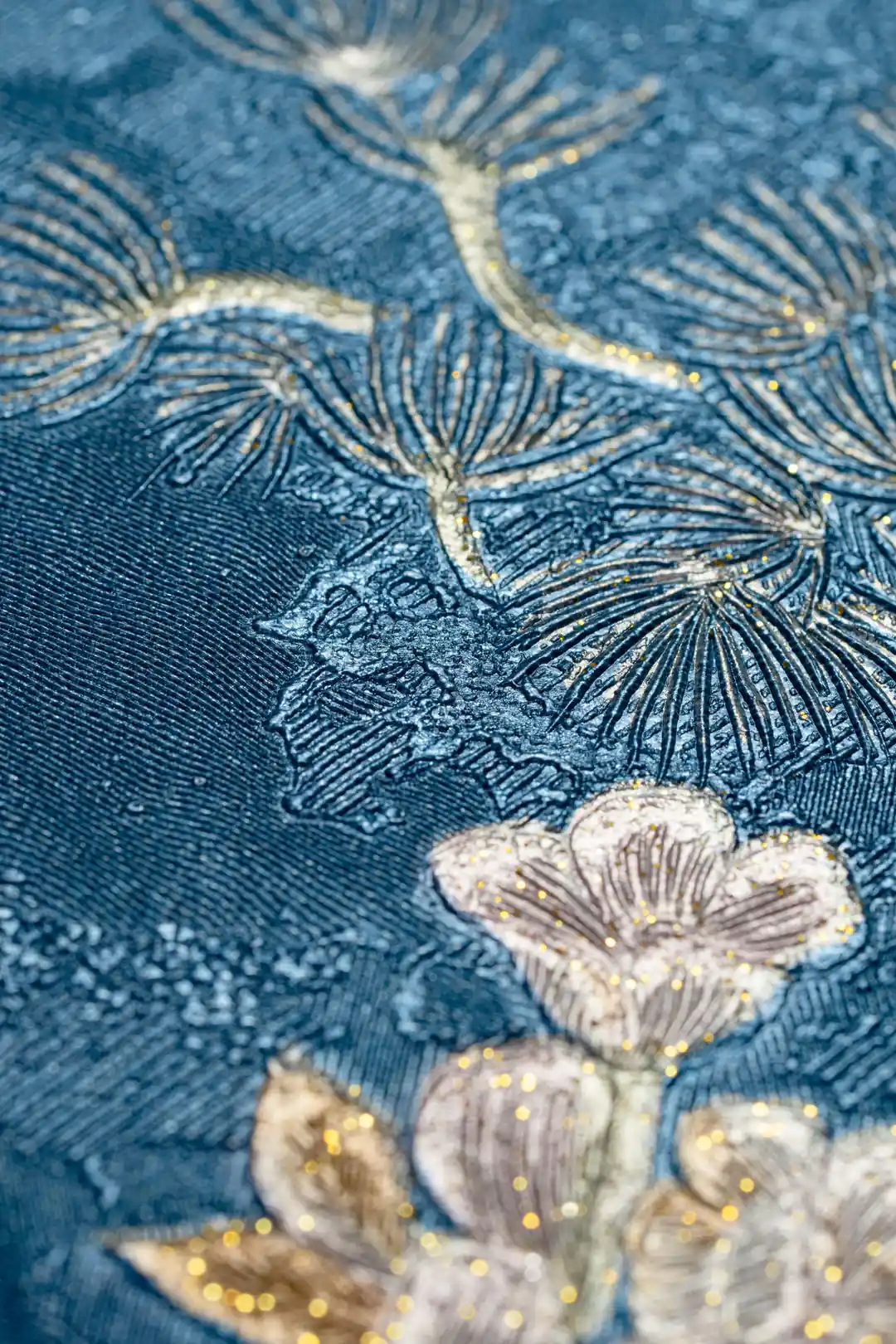 Macro detail of embossed pine needle and flower texture with gold glitter on deep blue wallpaper