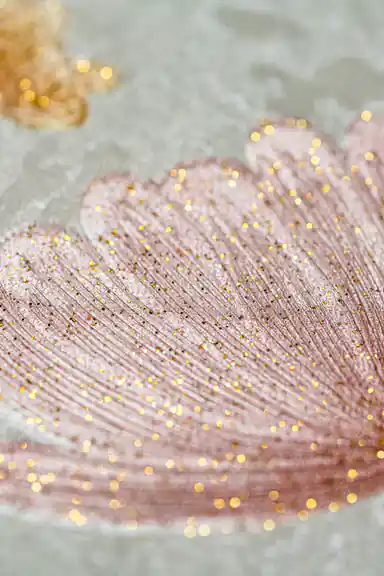 Extreme macro of a glittery pink flower petal with gold sparkle dots on light grey wallpaper surface