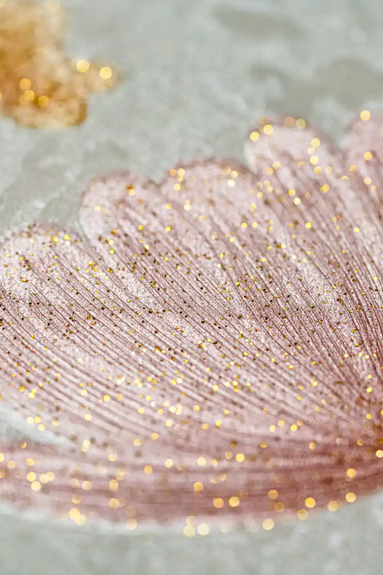 Extreme macro of a glittery pink flower petal with gold sparkle dots on light grey wallpaper surface