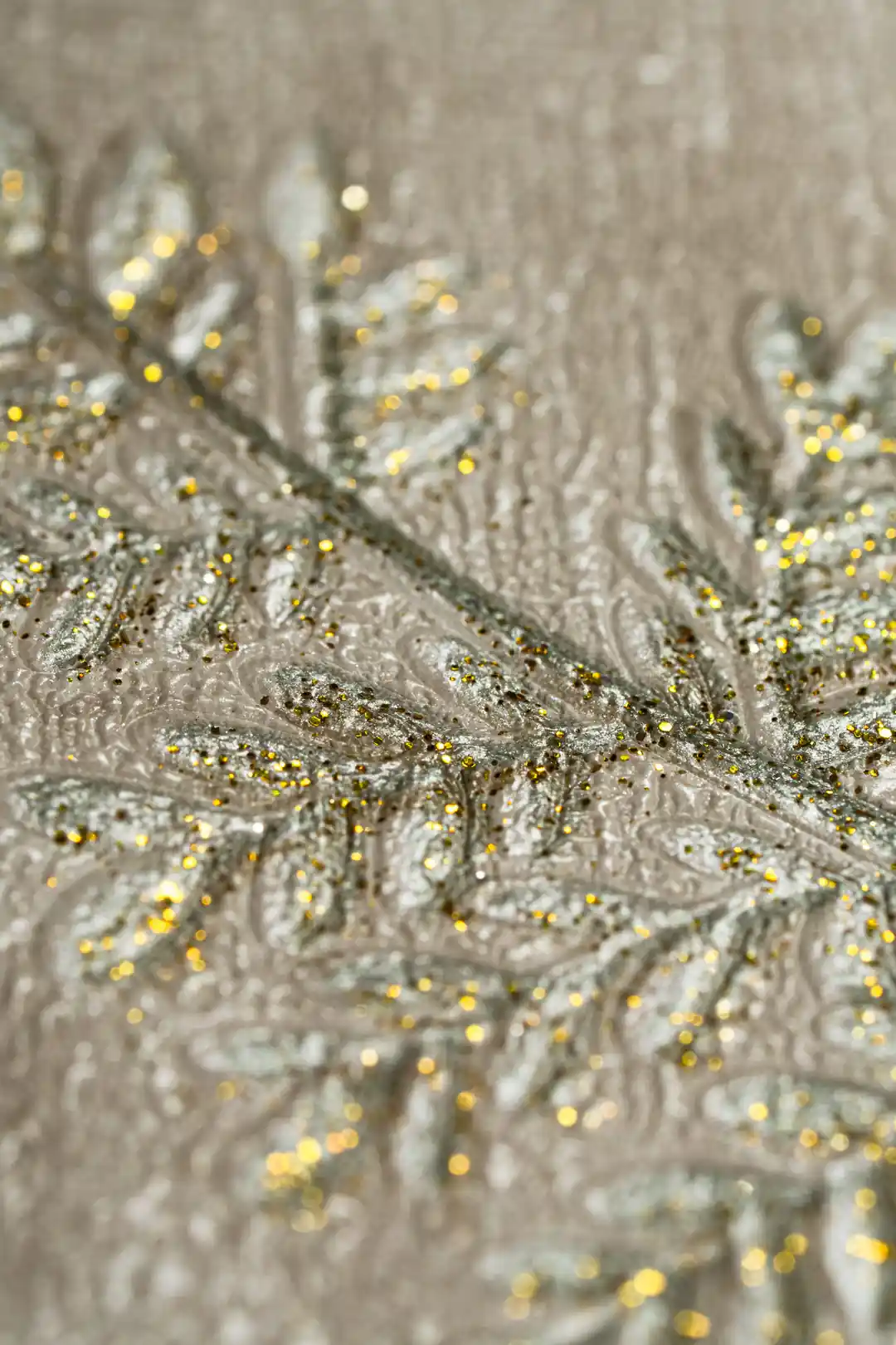 Extreme macro of embossed gold glitter fern leaf detail on the beige textured wallpaper surface