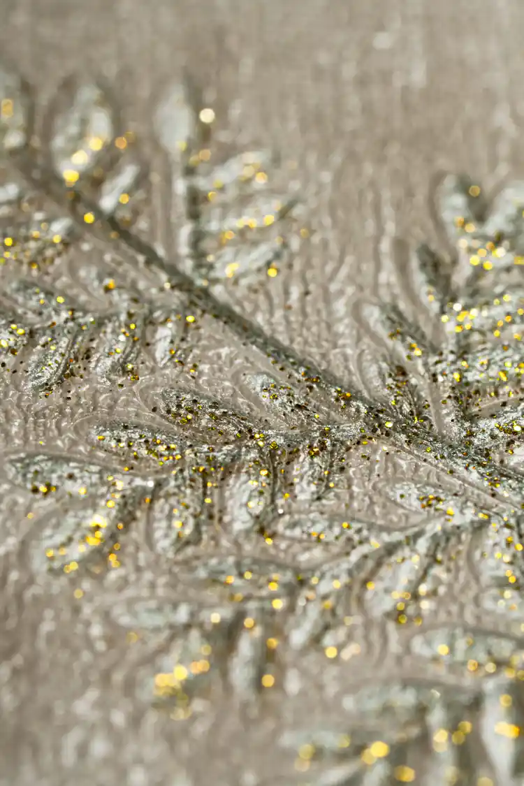 Extreme macro of embossed gold glitter fern leaf detail on the beige textured wallpaper surface