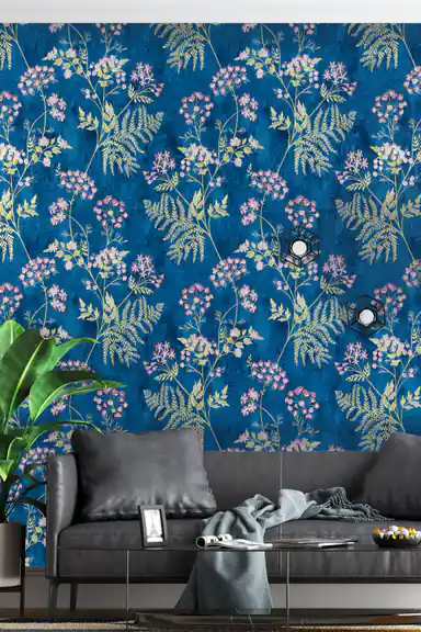 Living room with royal blue botanical wallpaper behind a grey leather sofa, banana plant, and wall lights