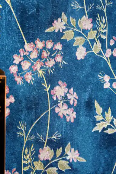 Close-up of delicate pink flower clusters with golden leaves on the deep blue textured wallpaper surface