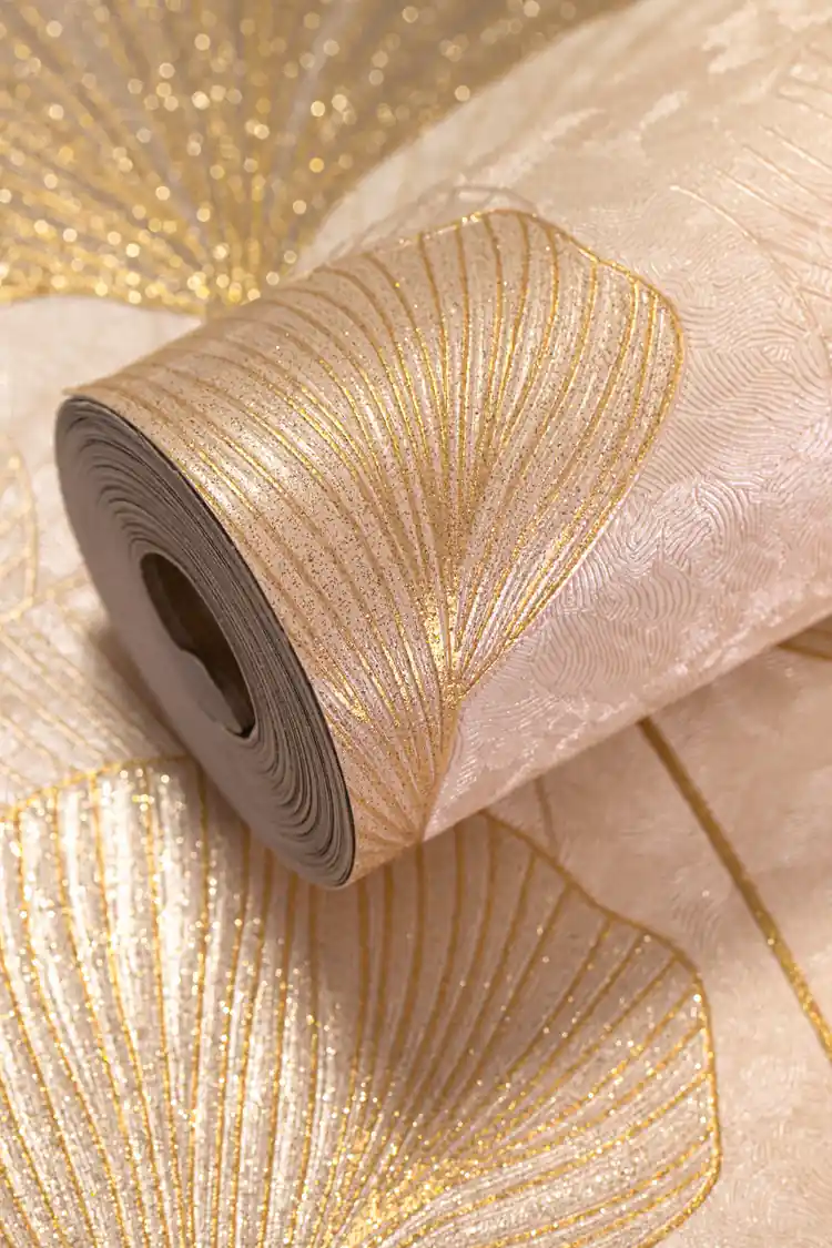 Rolled beige wallpaper with golden ginkgo leaf pattern and heavy glitter finish on a flat-lay surface