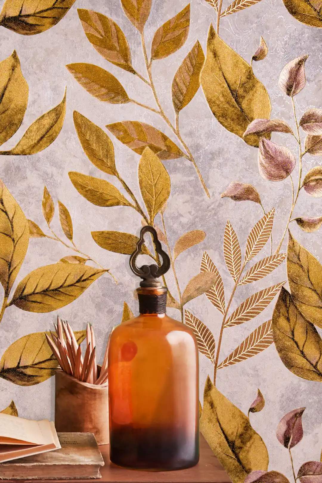 Close-up of golden shimmer leaves wallpaper with an amber glass bottle and books on a wooden shelf