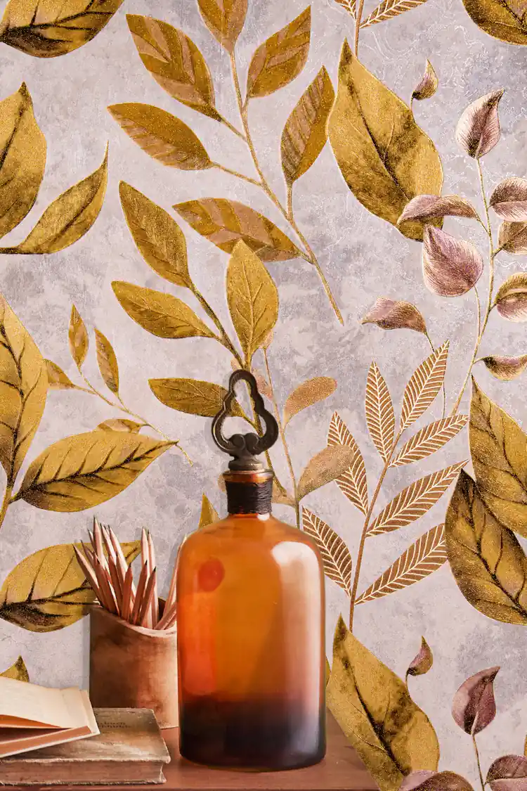 Close-up of golden shimmer leaves wallpaper with an amber glass bottle and books on a wooden shelf