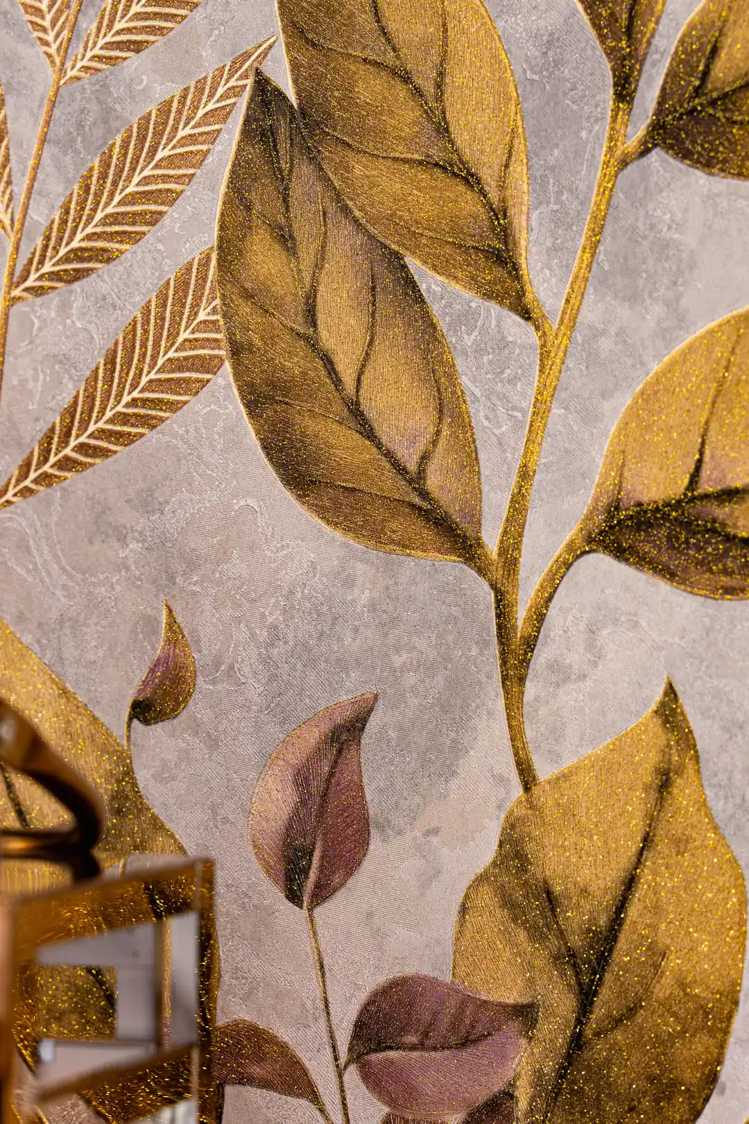 Detailed view of golden and mauve botanical leaves on textured grey wallpaper with visible vein details