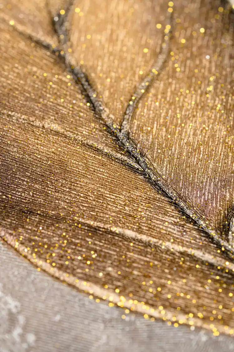 Extreme close-up of a single golden leaf showing glitter shimmer texture and dark veining on grey base