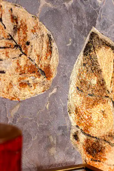 Detailed view of individual brown leaves with golden glitter texture on marbled mauve wallpaper surface