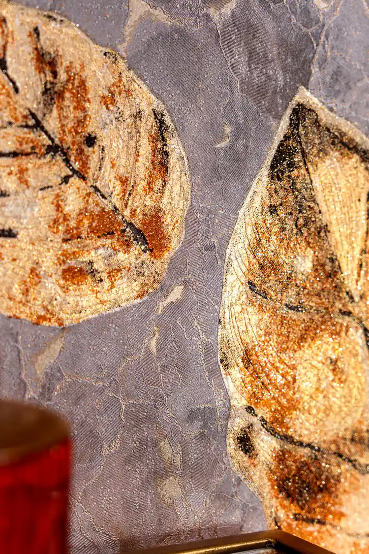Detailed view of individual brown leaves with golden glitter texture on marbled mauve wallpaper surface