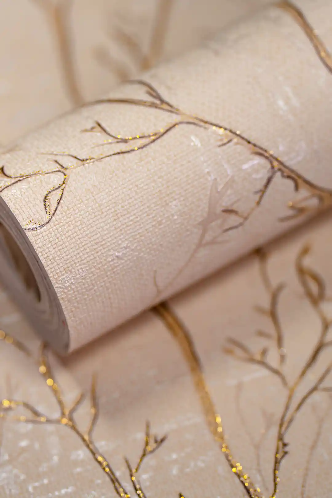 Rolled beige wallpaper with delicate gold glitter tree branch pattern on a textured cream base