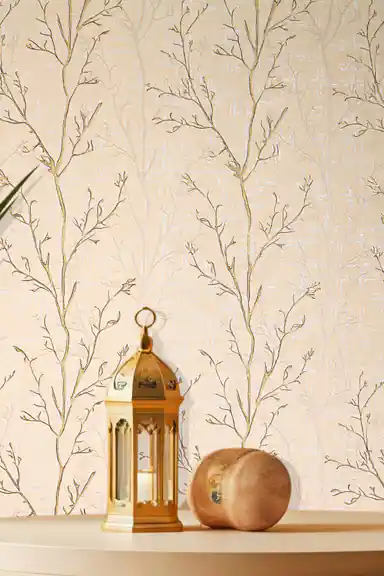 Close-up of gold glitter branch wallpaper with a brass Moroccan lantern and decorative wooden sphere