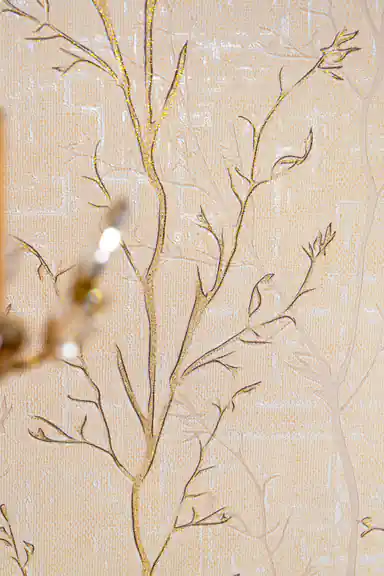 Detailed view of gold-outlined bare branches with glitter accents on cream textured wallpaper