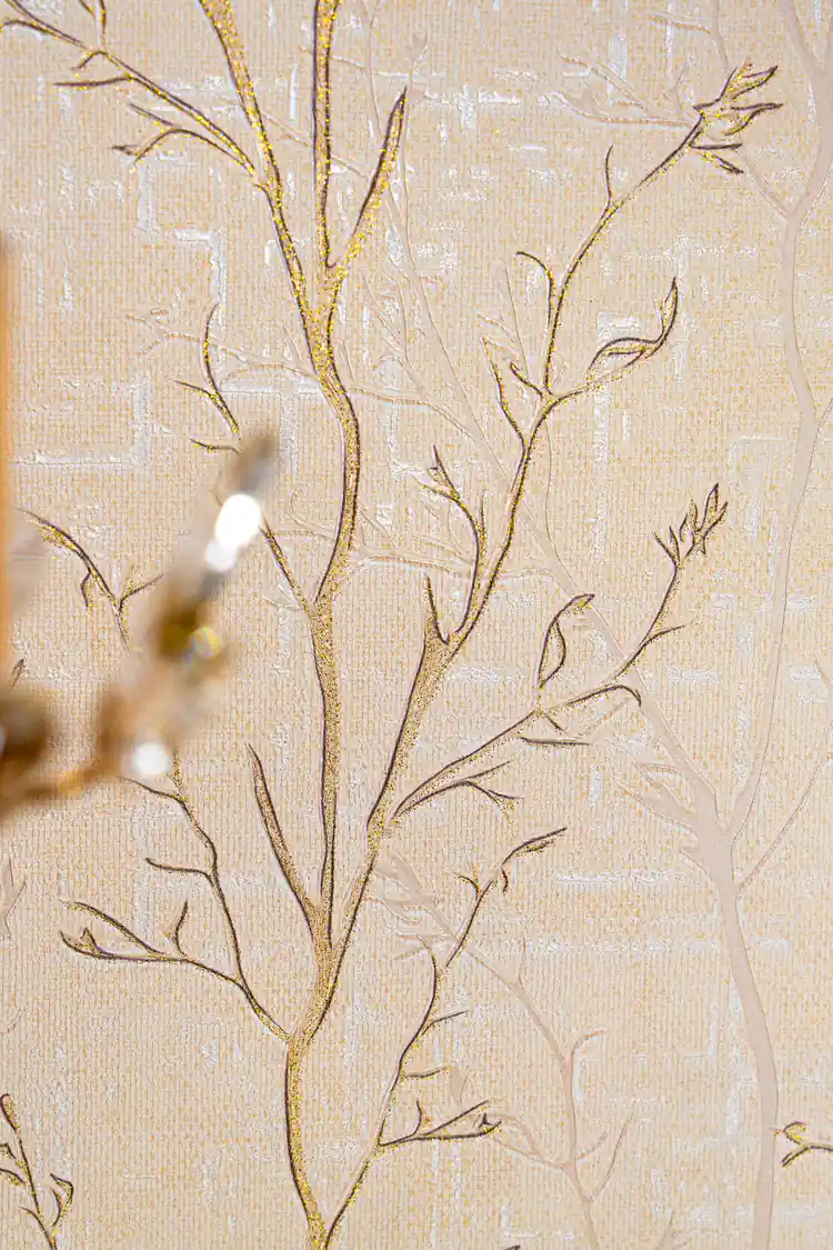 Detailed view of gold-outlined bare branches with glitter accents on cream textured wallpaper