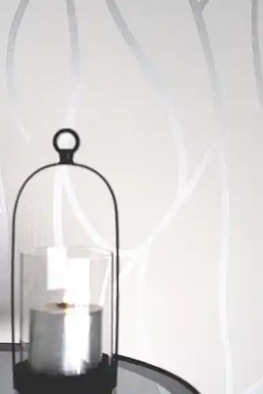 Close-up of white wallpaper with silver abstract branch lines and a glass cloche candle holder on a dark table