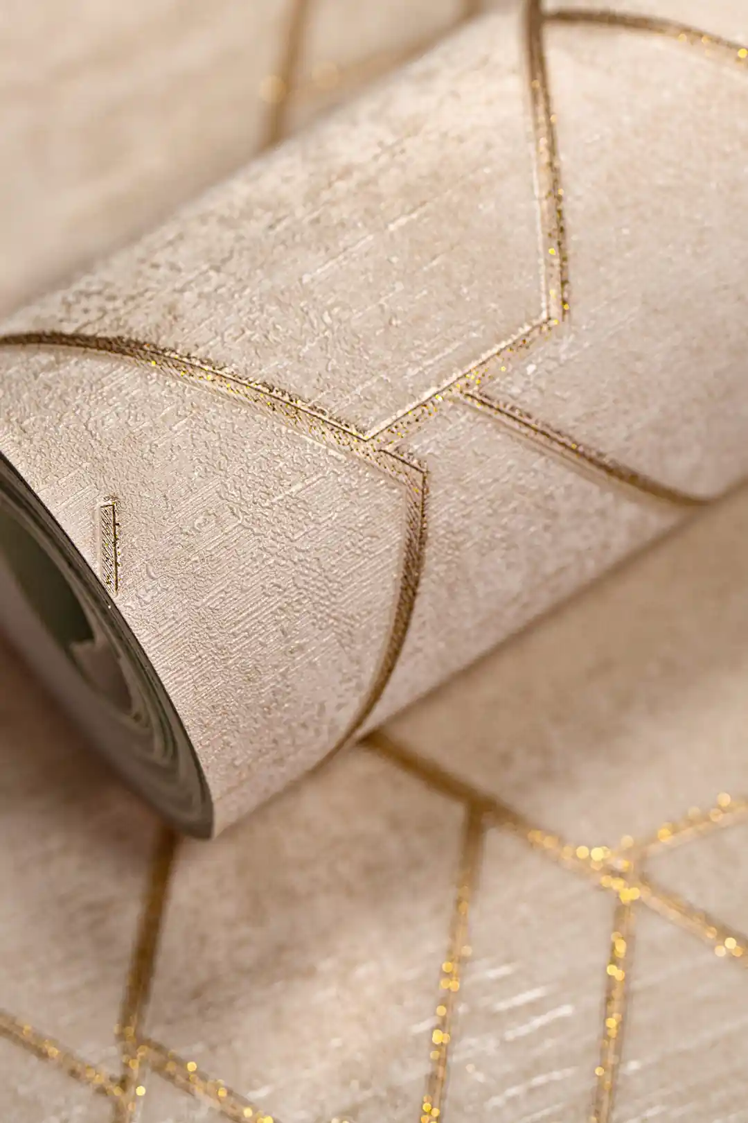 Rolled beige wallpaper with geometric hexagonal pattern outlined in gold glitter lines on a textured base