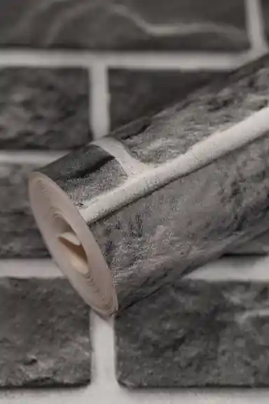 Rolled charcoal grey stone brick wallpaper showing realistic brick pattern with white mortar lines