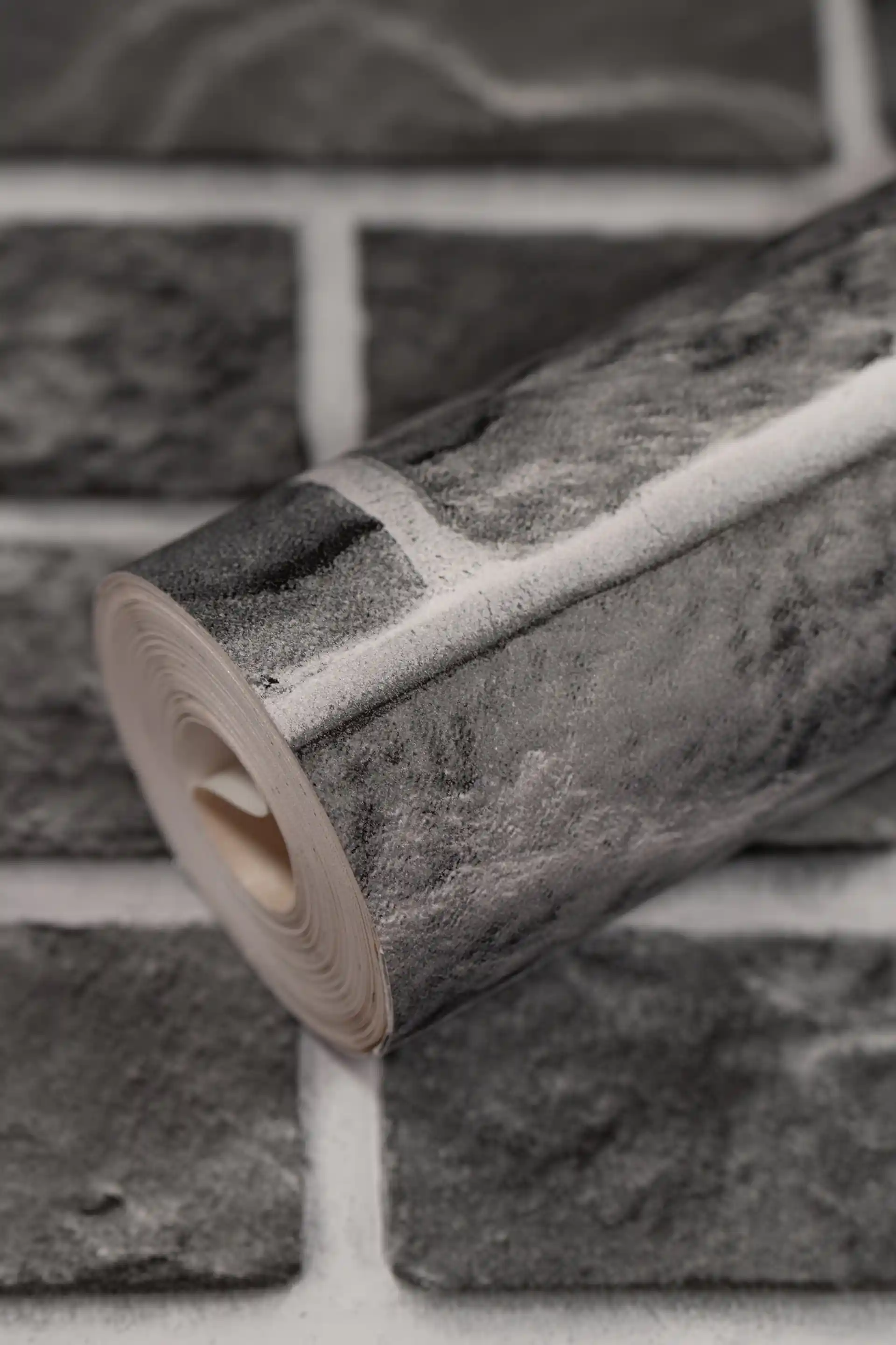 Rolled charcoal grey stone brick wallpaper showing realistic brick pattern with white mortar lines