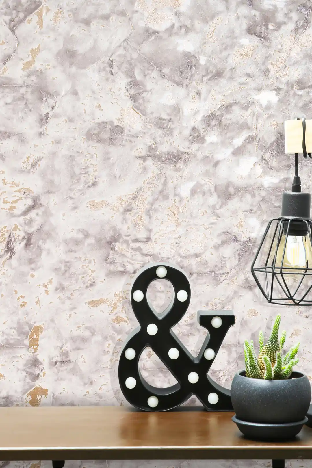 Close-up of grey marble wallpaper with gold accents and decorative ampersand marquee light on a shelf