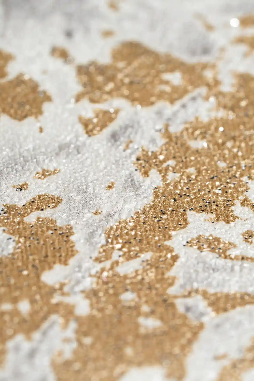 Extreme macro of gold foil glitter flecks scattered across grey marble wallpaper surface