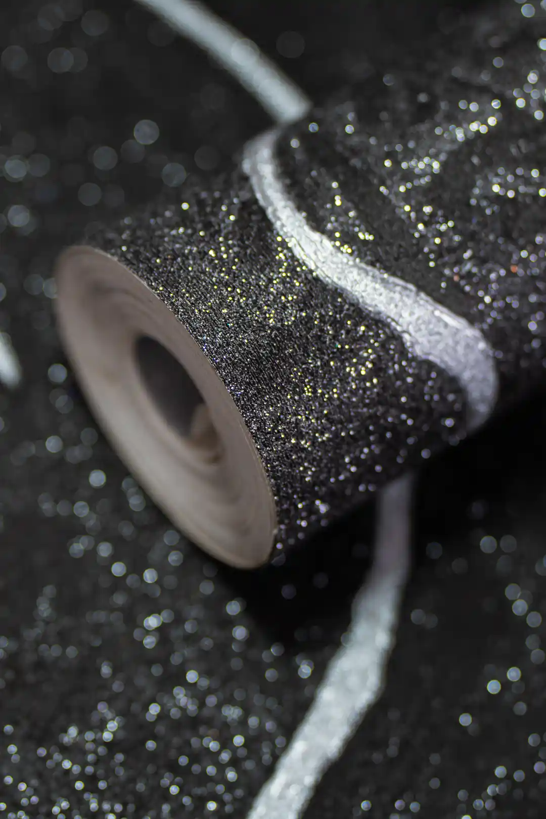 Rolled black glitter wallpaper with silver metallic accent lines on a sparkling dark textured surface