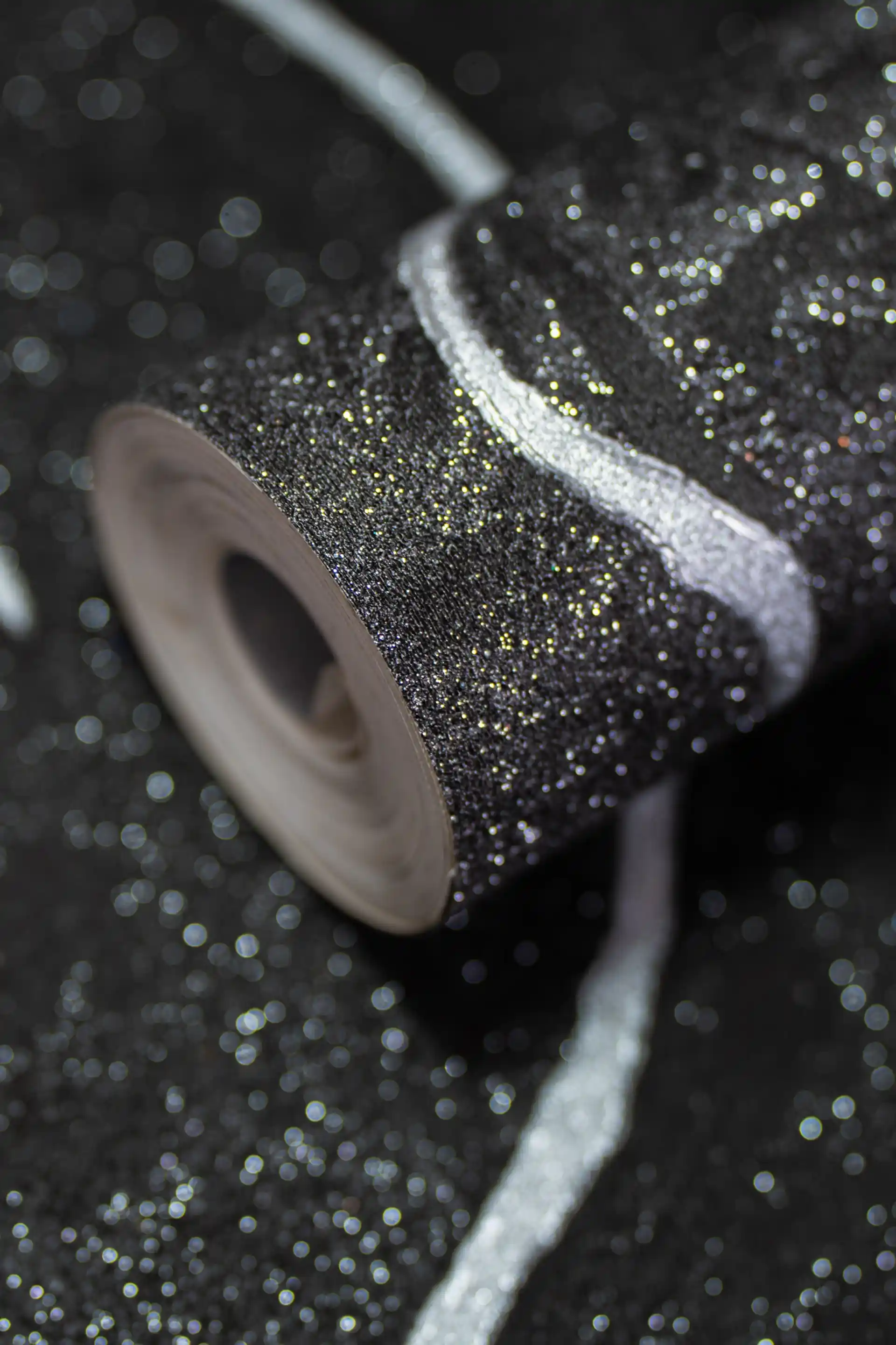 Rolled black glitter wallpaper with silver metallic accent lines on a sparkling dark textured surface