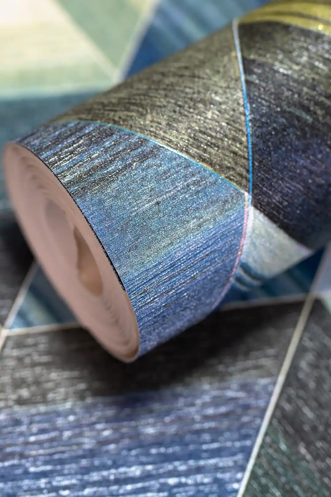 Rolled wallpaper with 3D geometric triangle tiles in blue, green, and gold tones on a textured surface