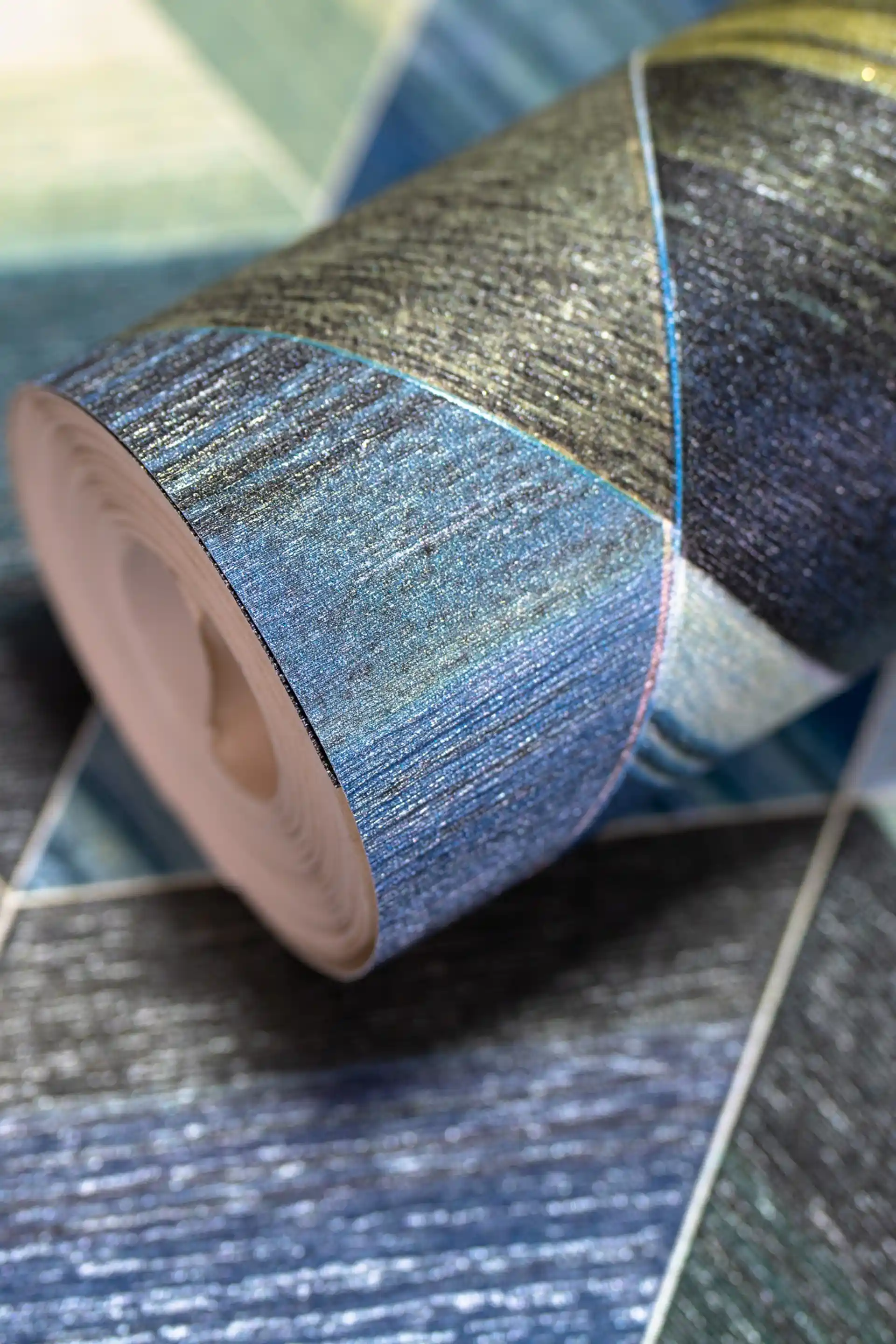 Rolled wallpaper with 3D geometric triangle tiles in blue, green, and gold tones on a textured surface