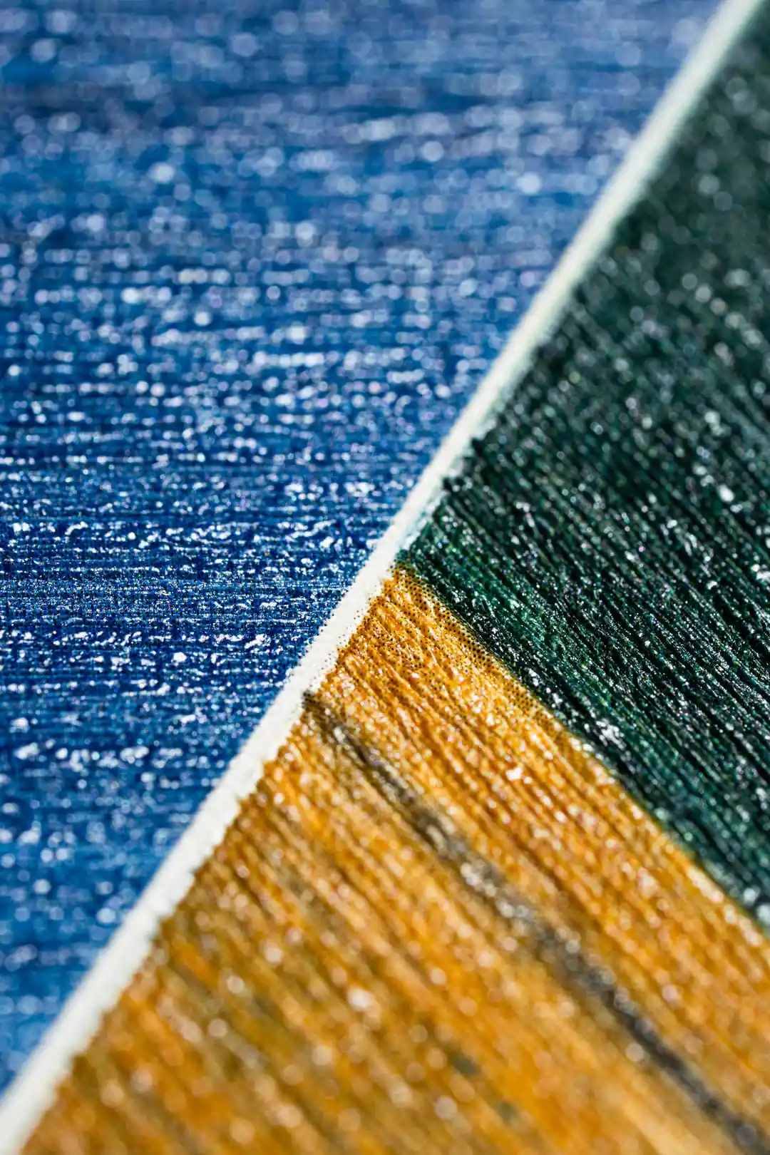 Extreme close-up of blue, green, and gold hexagonal tile wallpaper showing brushed texture detail