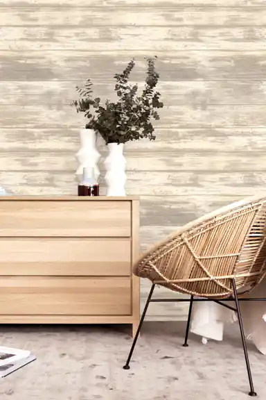 Distressed wood plank wallpaper in a bohemian room with a natural oak dresser and rattan lounge chair