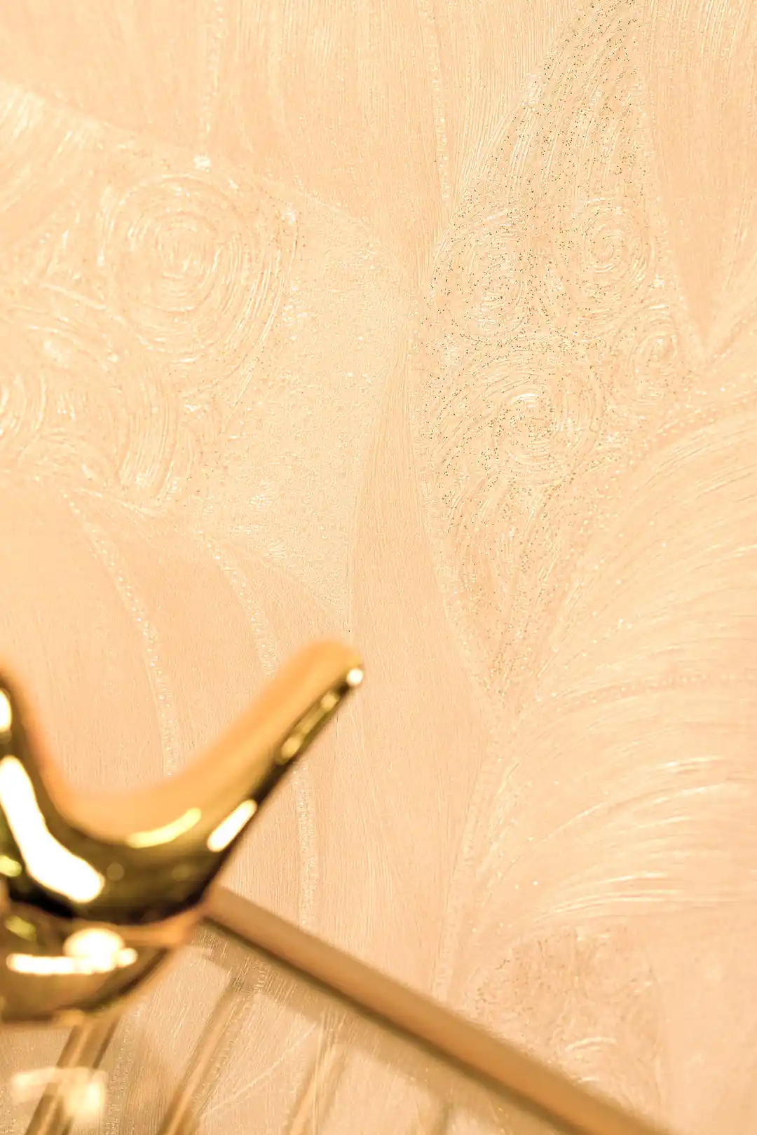 Detailed view of embossed swirl pattern on beige-gold wallpaper with a decorative gold bird accent