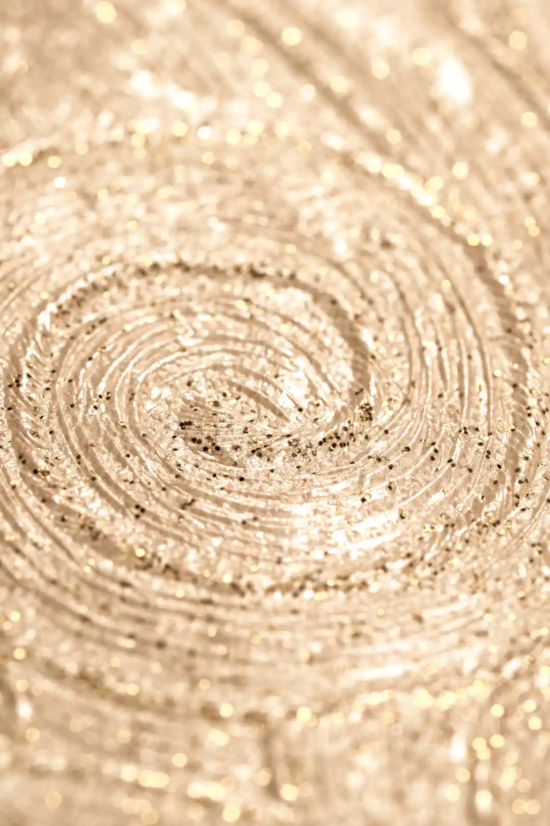 Extreme macro of gold glitter swirl detail showing the sparkling concentric pattern on beige wallpaper