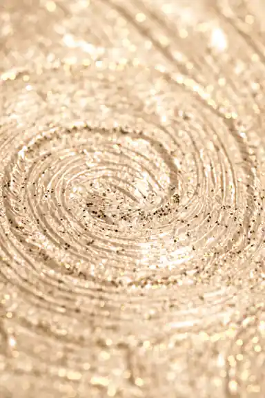 Extreme macro of gold glitter swirl detail showing the sparkling concentric pattern on beige wallpaper