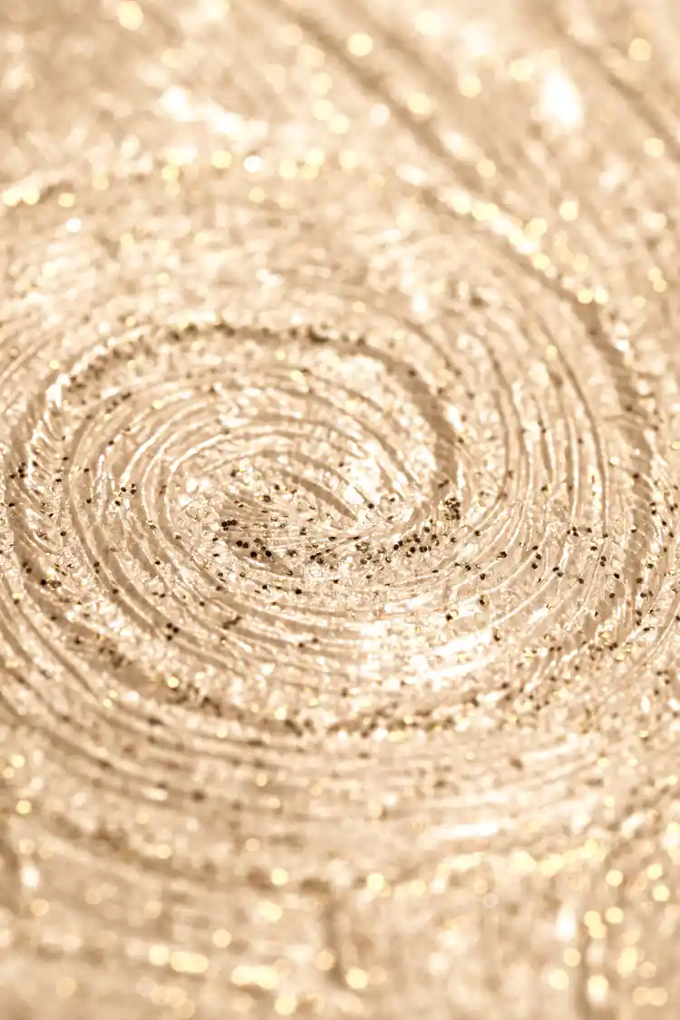 Extreme macro of gold glitter swirl detail showing the sparkling concentric pattern on beige wallpaper