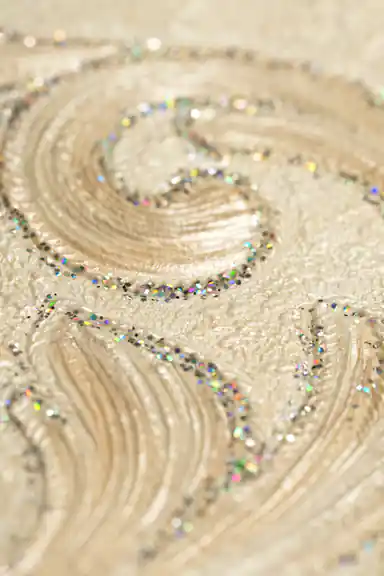 Extreme close-up of embossed damask scroll with holographic rainbow glitter on ivory wallpaper