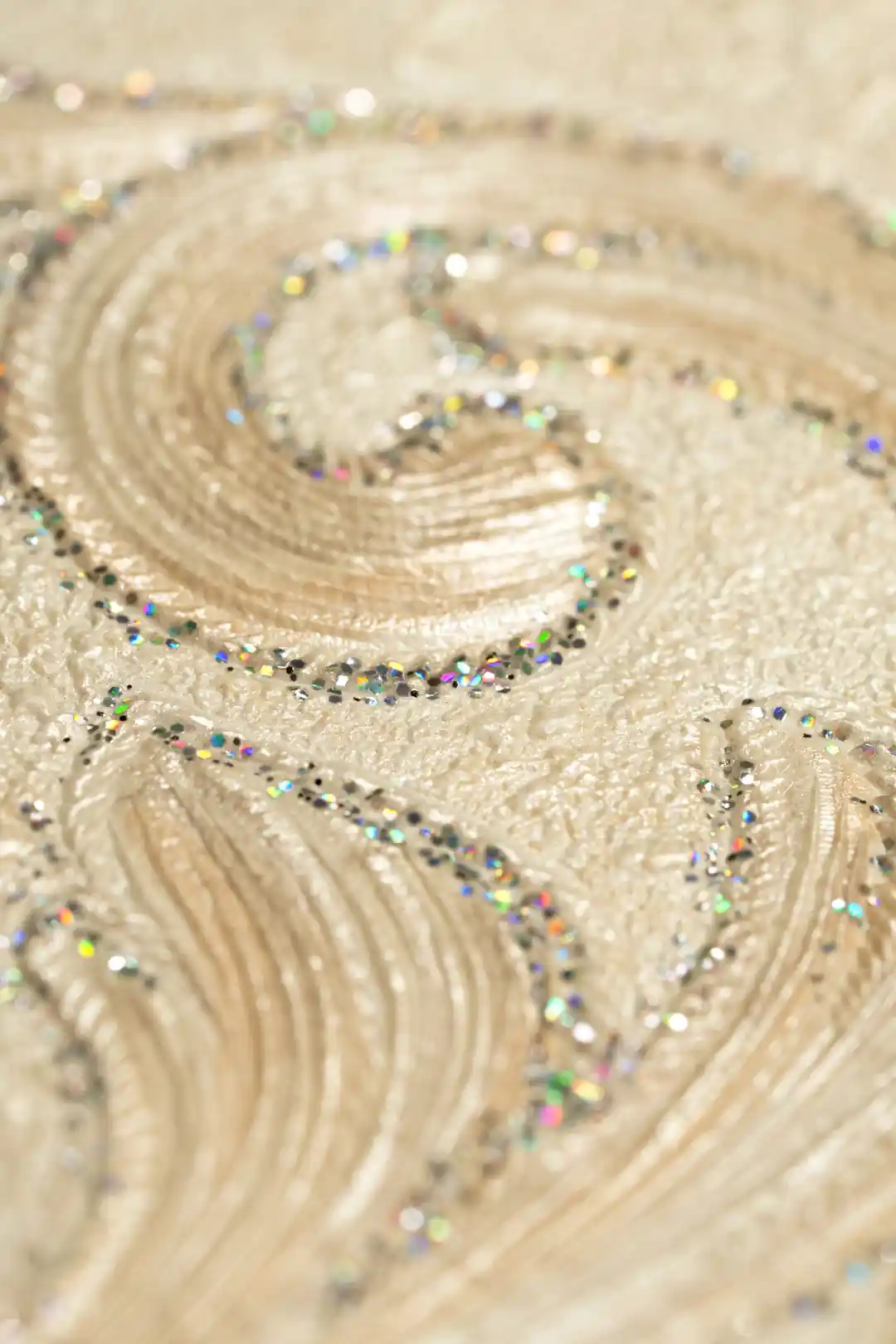 Extreme close-up of embossed damask scroll with holographic rainbow glitter on ivory wallpaper