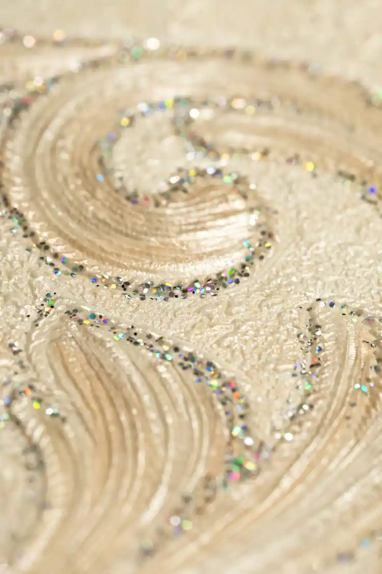 Extreme close-up of embossed damask scroll with holographic rainbow glitter on ivory wallpaper