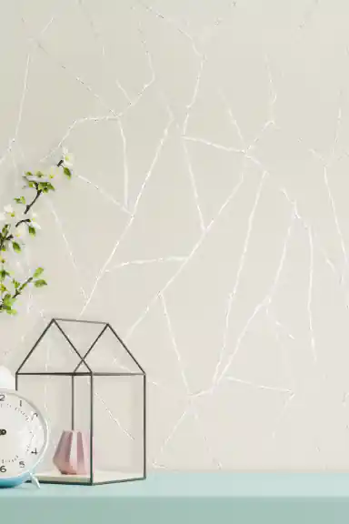 Off-white textured wallpaper with shimmering silver abstract vein lines displayed on a styled shelf