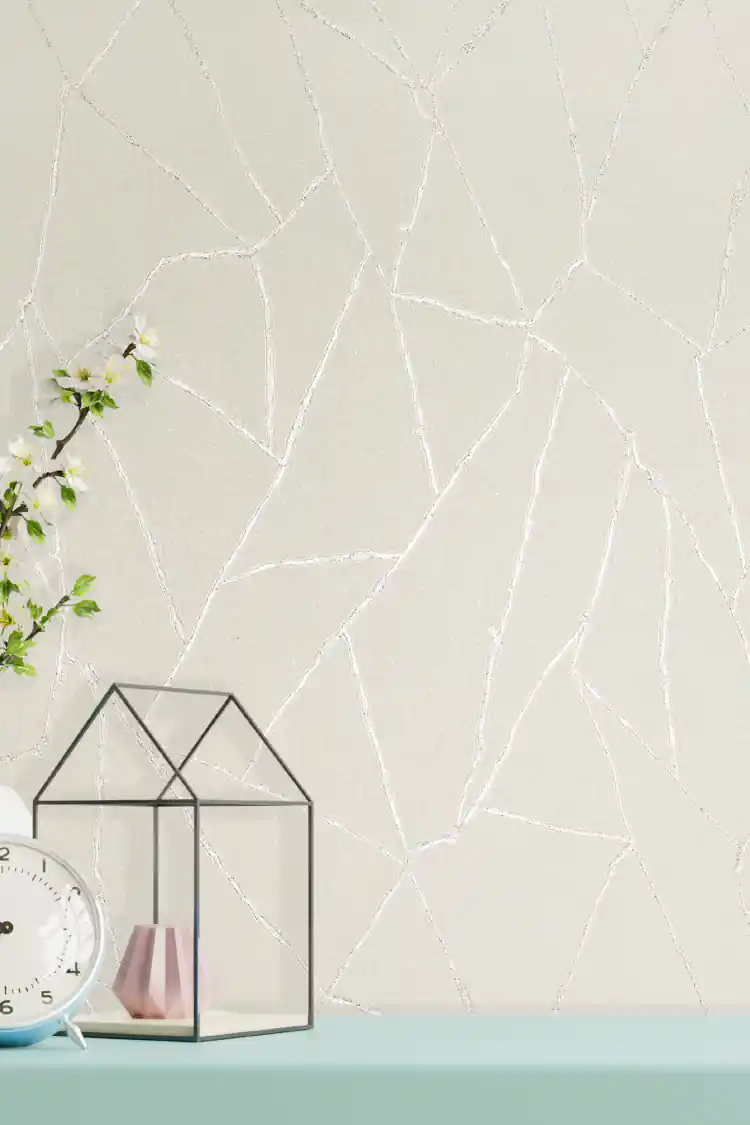 Off-white textured wallpaper with shimmering silver abstract vein lines displayed on a styled shelf
