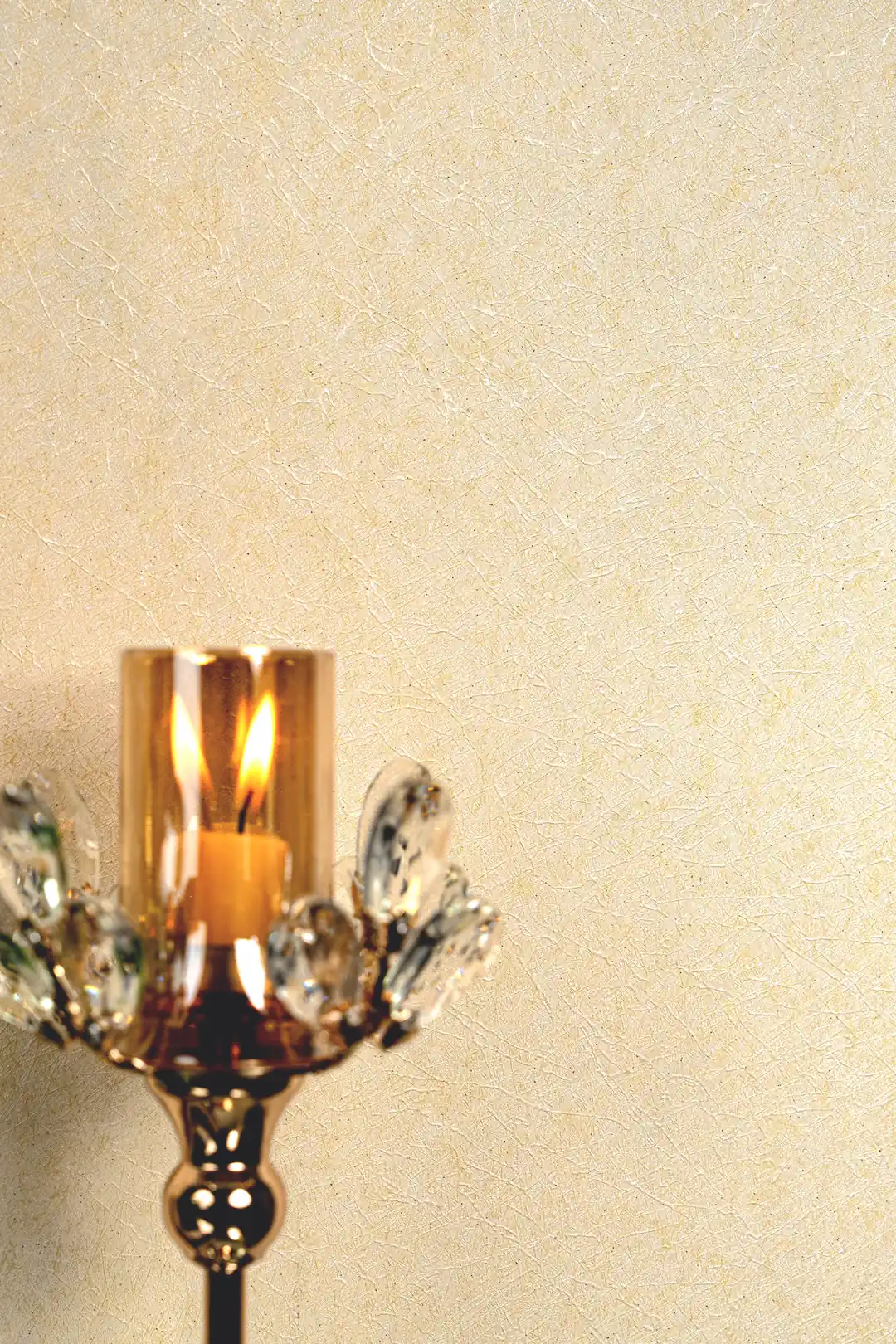 Warm close-up of cream silk wallpaper with lit candle in crystal holder showing soft shimmer